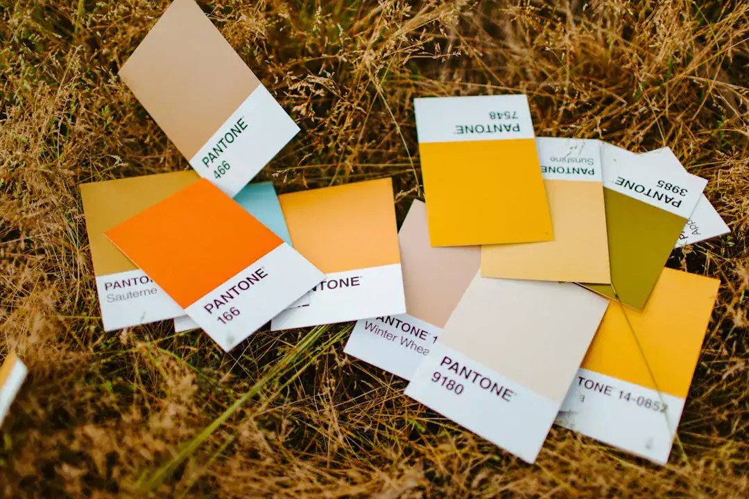 Pantone color swatches scattered on dry grass with yellow, orange, and beige tones