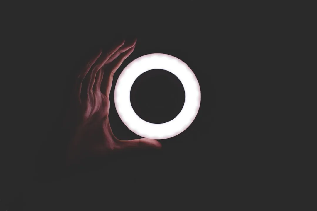 Hand holding a glowing circular ring light in a dark background.