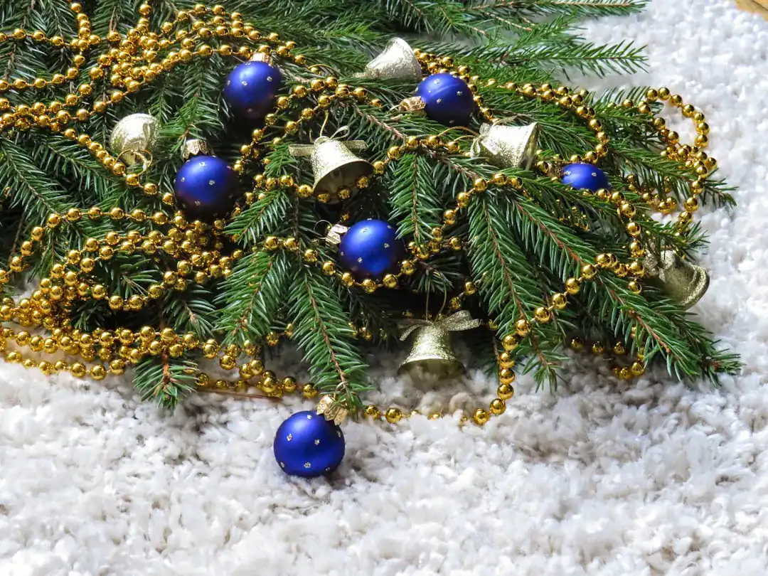 Evergreen branches with blue ornaments, bells and gold beads on snowy surface