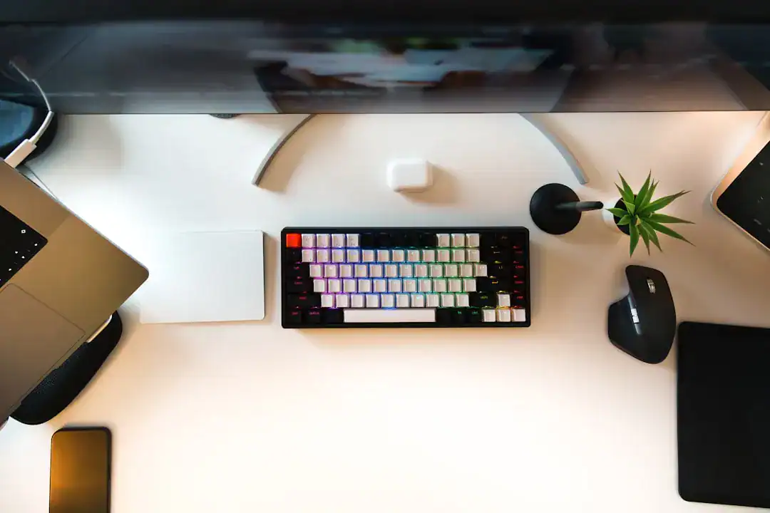 Top-down view of a modern desk with colorful RGB keyboard, laptop, mouse, smartphone and plant