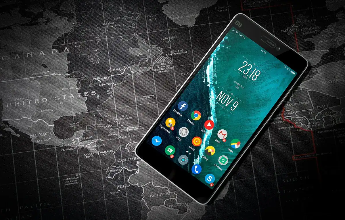 Smartphone with app icons on its home screen laid over a dark world map background.