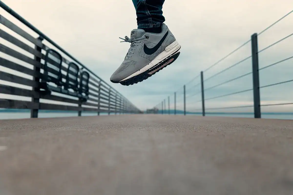 Close-up of a gray Nike running shoe in mid-air on a wooden pier with railings