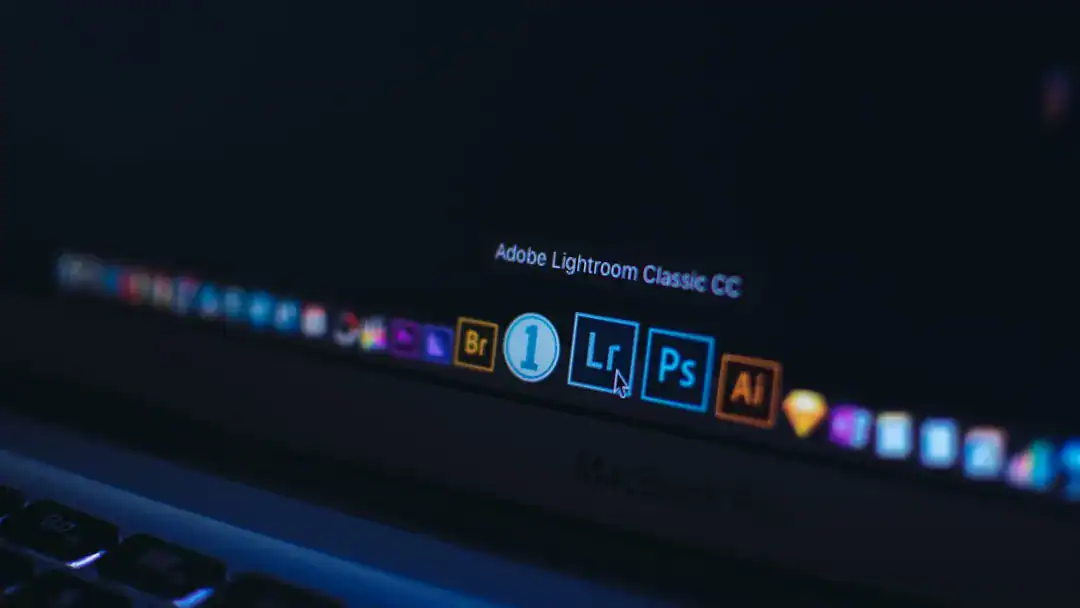 Dark MacBook Pro screen showing glowing Adobe Creative Cloud icons on the dock (Bridge, Lightroom, Photoshop, Illust