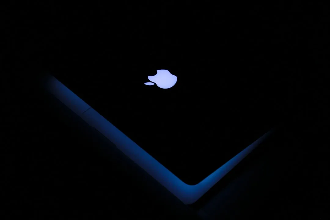 Glowing Apple logo on a dark laptop lid with blue edge lighting