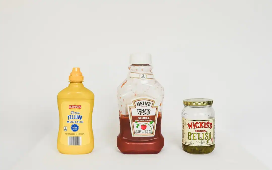 Mustard bottle, ketchup bottle, and relish jar on a white surface
