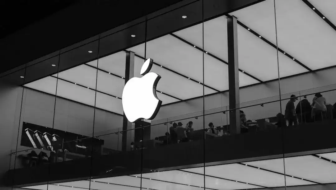 Large Apple logo on glass storefront with shoppers on a mezzanine.