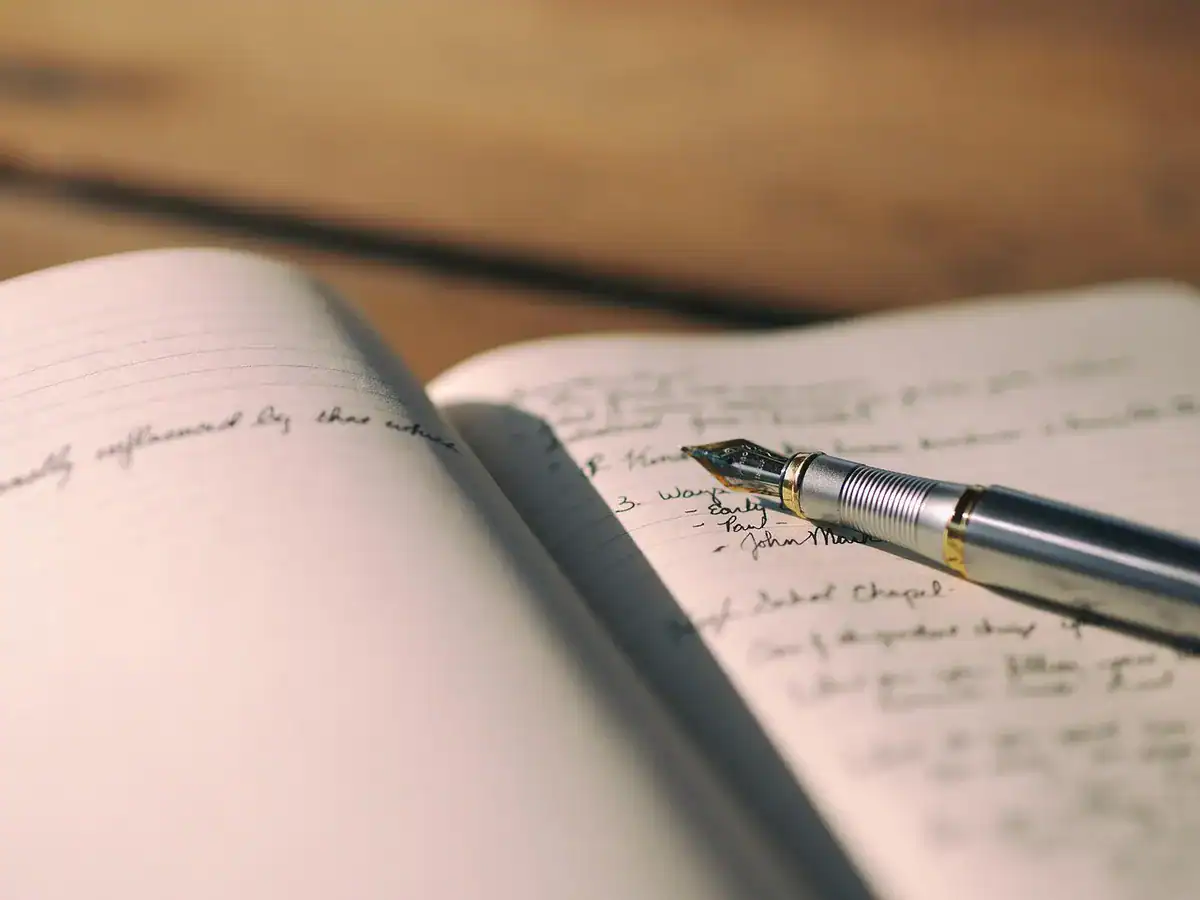 Open notebook with cursive notes and a fountain pen on a wooden desk