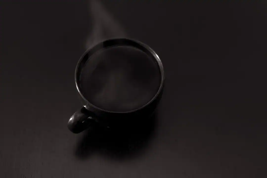 Steaming black coffee cup on a dark wooden surface