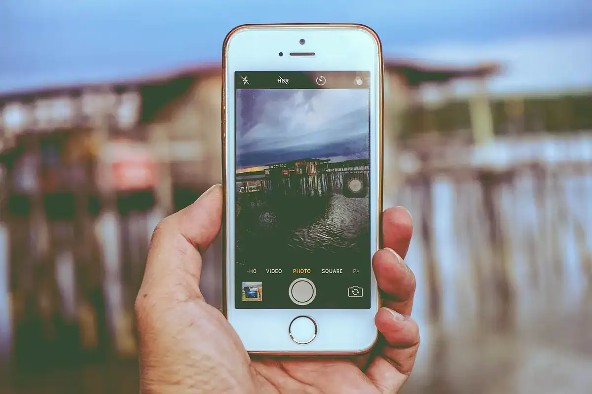 Hand holding iPhone photographing a wooden pier by the water